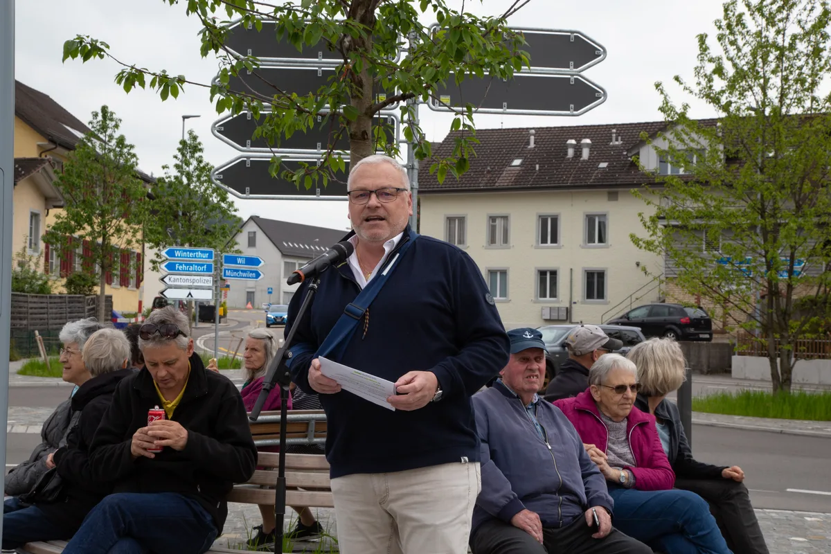 Gemeindepräsident René Gubler hielt eine Rede an einem ungewohnten Ort. Man sieht einen Mann, der eine Rede hält. Hinter ihm sitzen Personen auf einer runden Sitzbank.